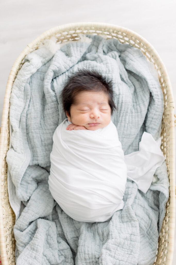 newborn baby laying in moses basket on blue blanket 