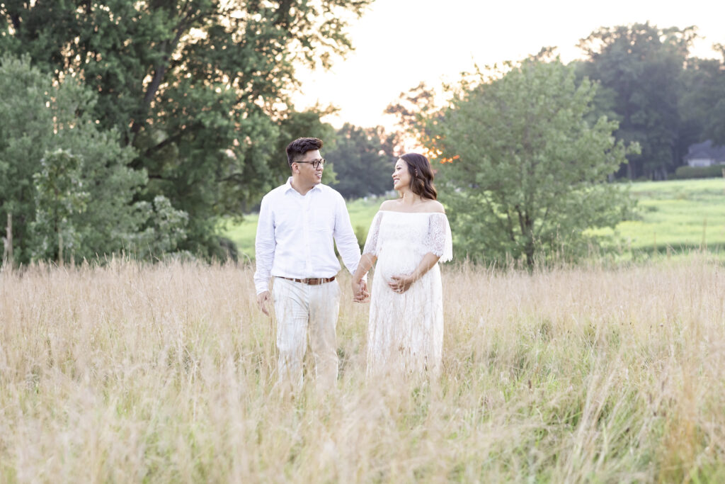 husband and wife walking through tall grass maternity portraits