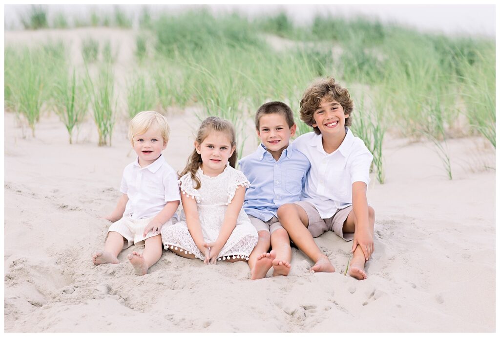 four siblings sitting on the beach for a family photograph