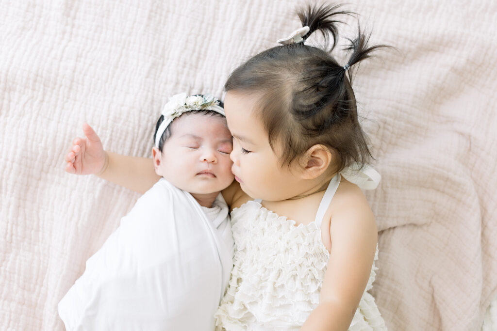 big sister kissing newborn baby girl sibling photo shoot
