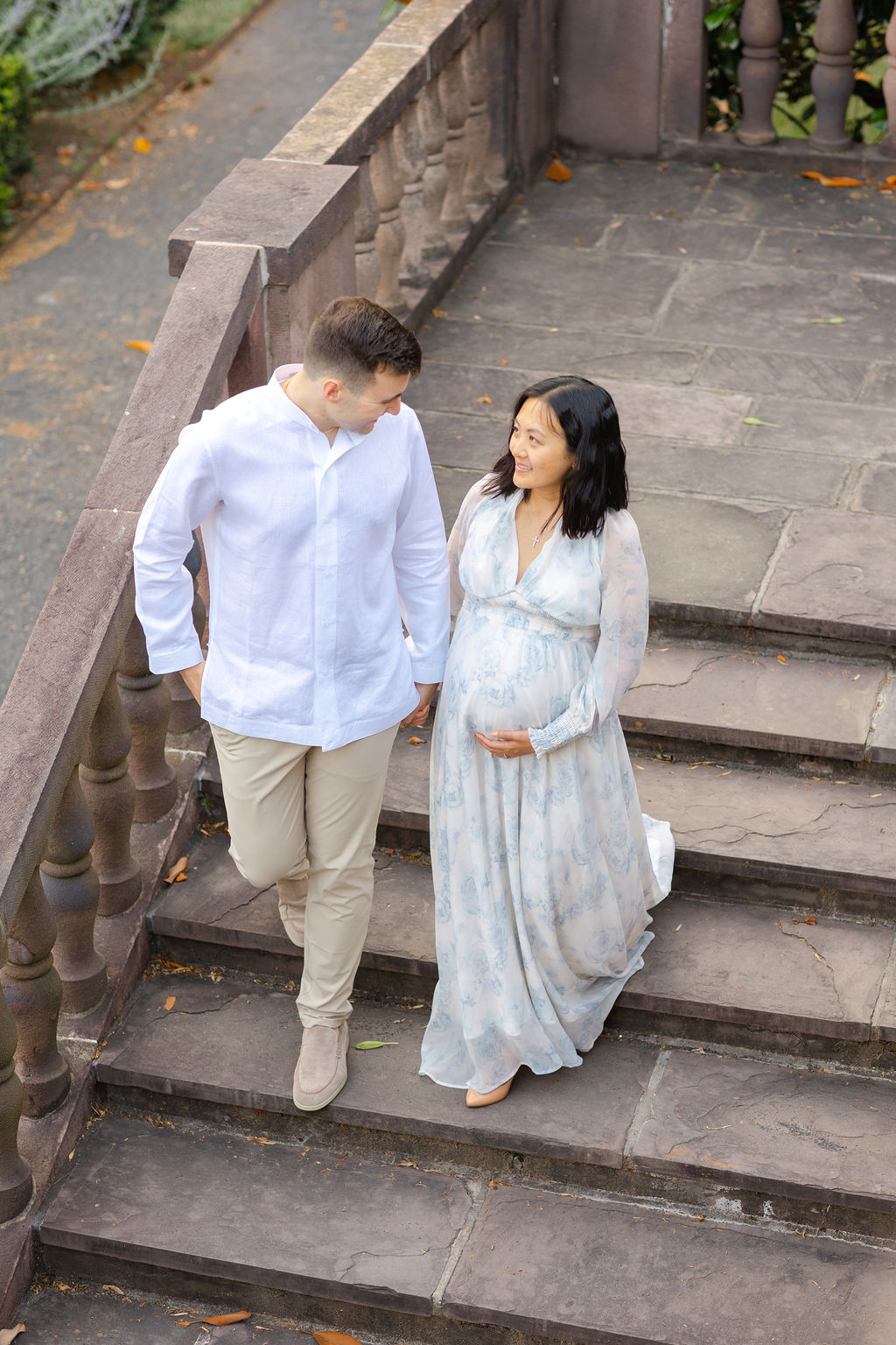 A mom to be in a blue maternity dress walks down some stone steps holding hands with her husband philadelphia prenatal massage