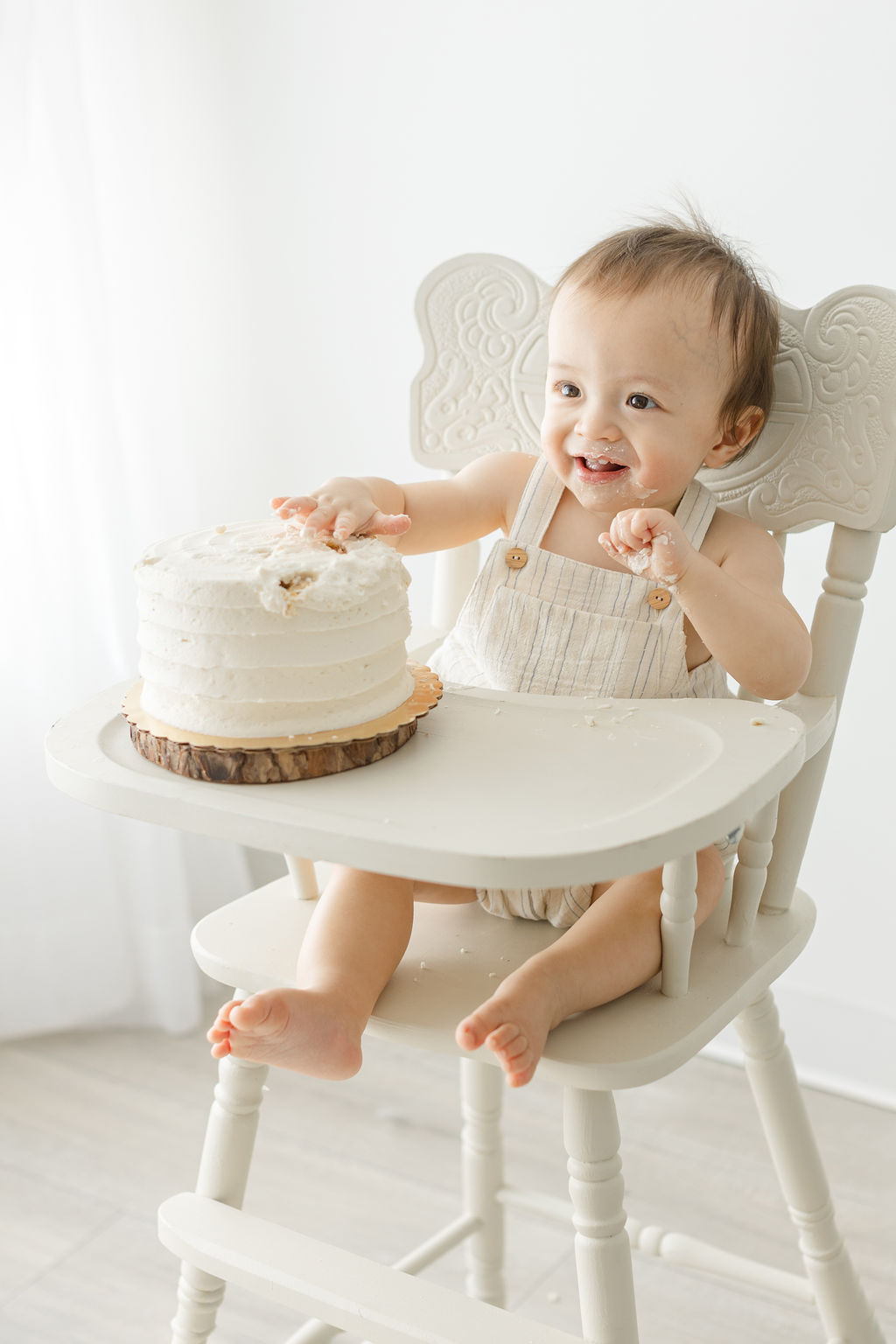 A toddler boy sits in a white high chair smashing a cake in a studio after attending mommy and me classes philadelphia