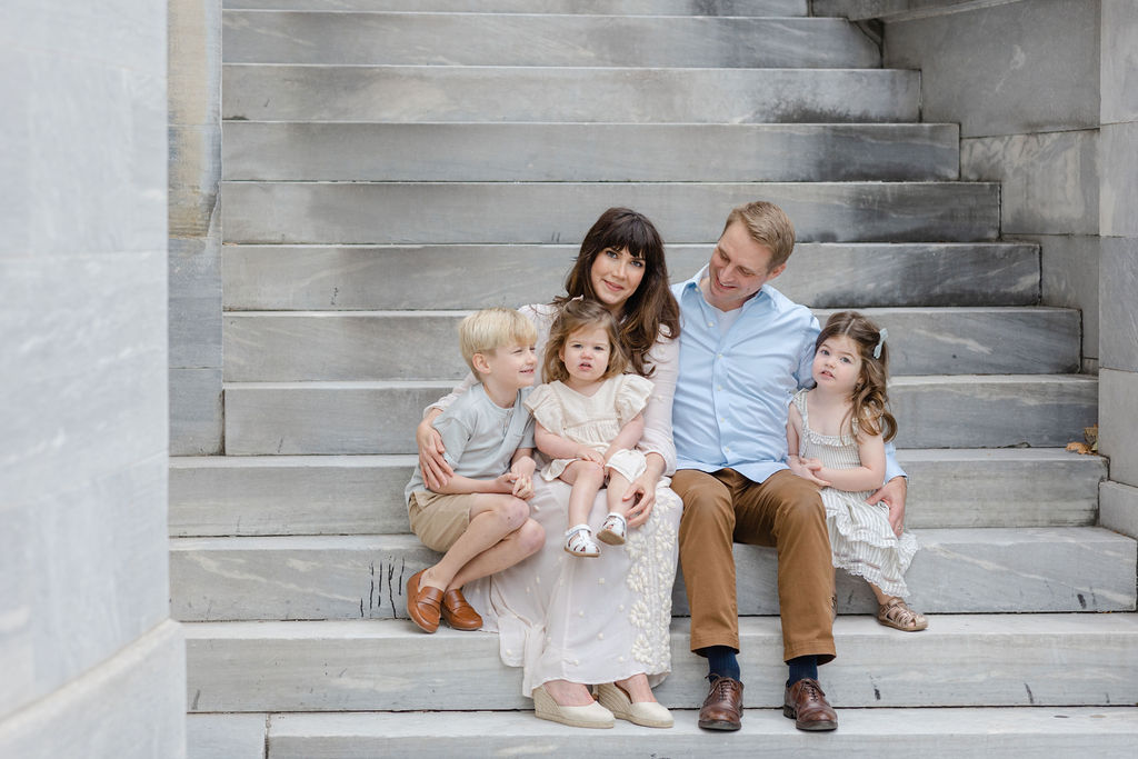 A family of 5 with three toddlers sit on a large marble staircase together before visiting family friendly restaurants philadelphia