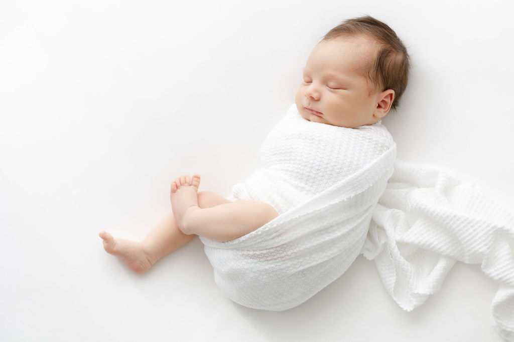 A newborn baby sleeps in a studio in a white swaddle thanks to doulas princeton nj
