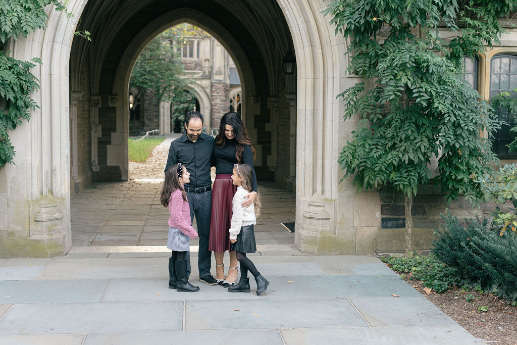 A mom and dad in black stand under a grand archway while hugging their two young daughters before visiting family friendly restaurants princeton