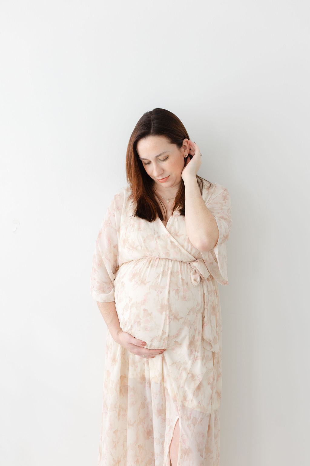 A mother to be stands against a wall in a studio smiling down to her bump thanks to a fertility clinic princeton nj