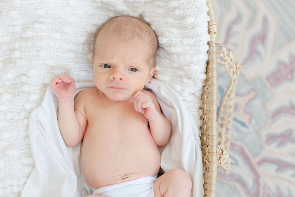 A Philadelphia lifestyle newborn photographer image of a newborn baby in a wicker basket and white blanket with eyes open