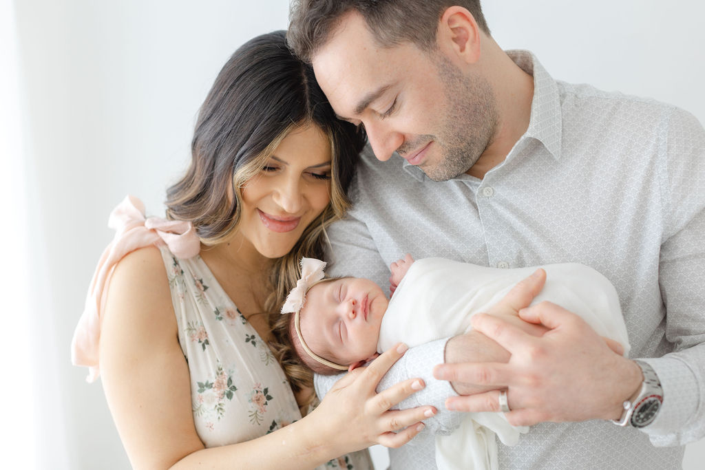 New mom and dad touch heads while dad cradles their sleeping newborn baby for a bucks county newborn photographer