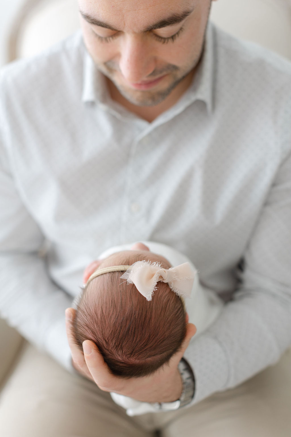 A new dad smiles down at his newborn daughter in his hands in front of him for a bucks county newborn photographer