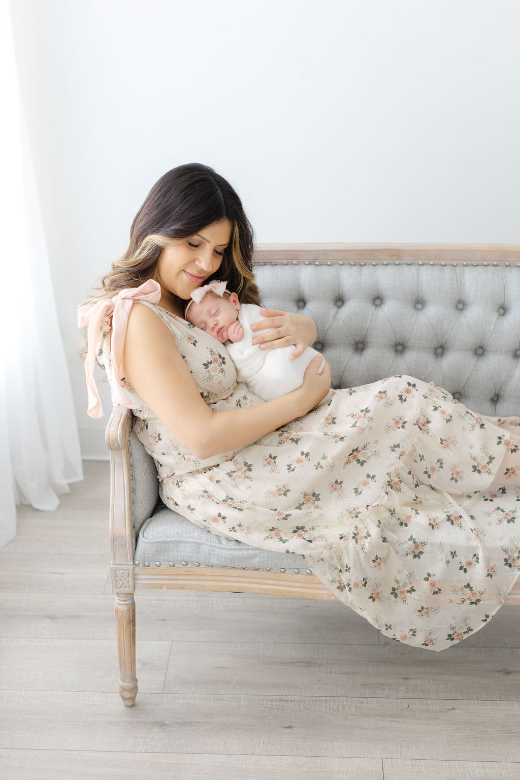 A happy new mother sits across a bench in a studio cradling her sleeping newborn daughter against her chest for a bucks county newborn photographer