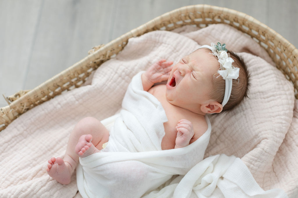 A newborn baby yawns while laying in a woven basket in the studio of a bucks county newborn photographer