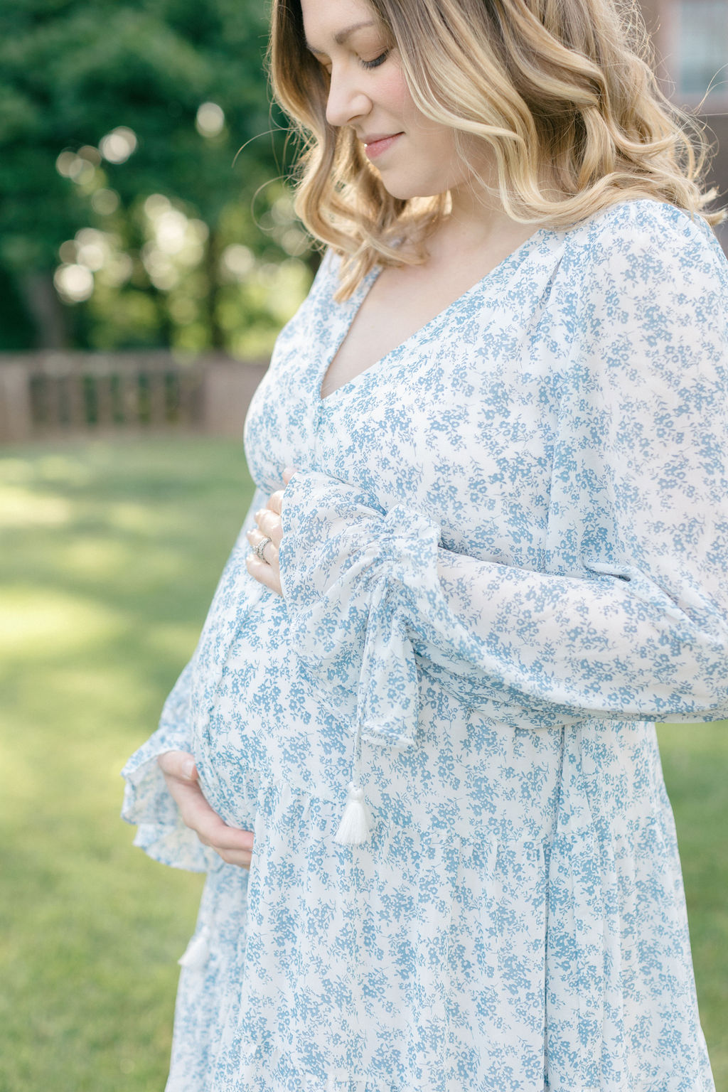 A mother to be in a blue maternity gown smiles down to her bump in a garden lawn