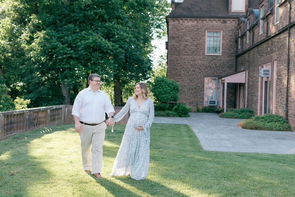 Happy expecting parents walk hand in hand through a garden lawn at sunset