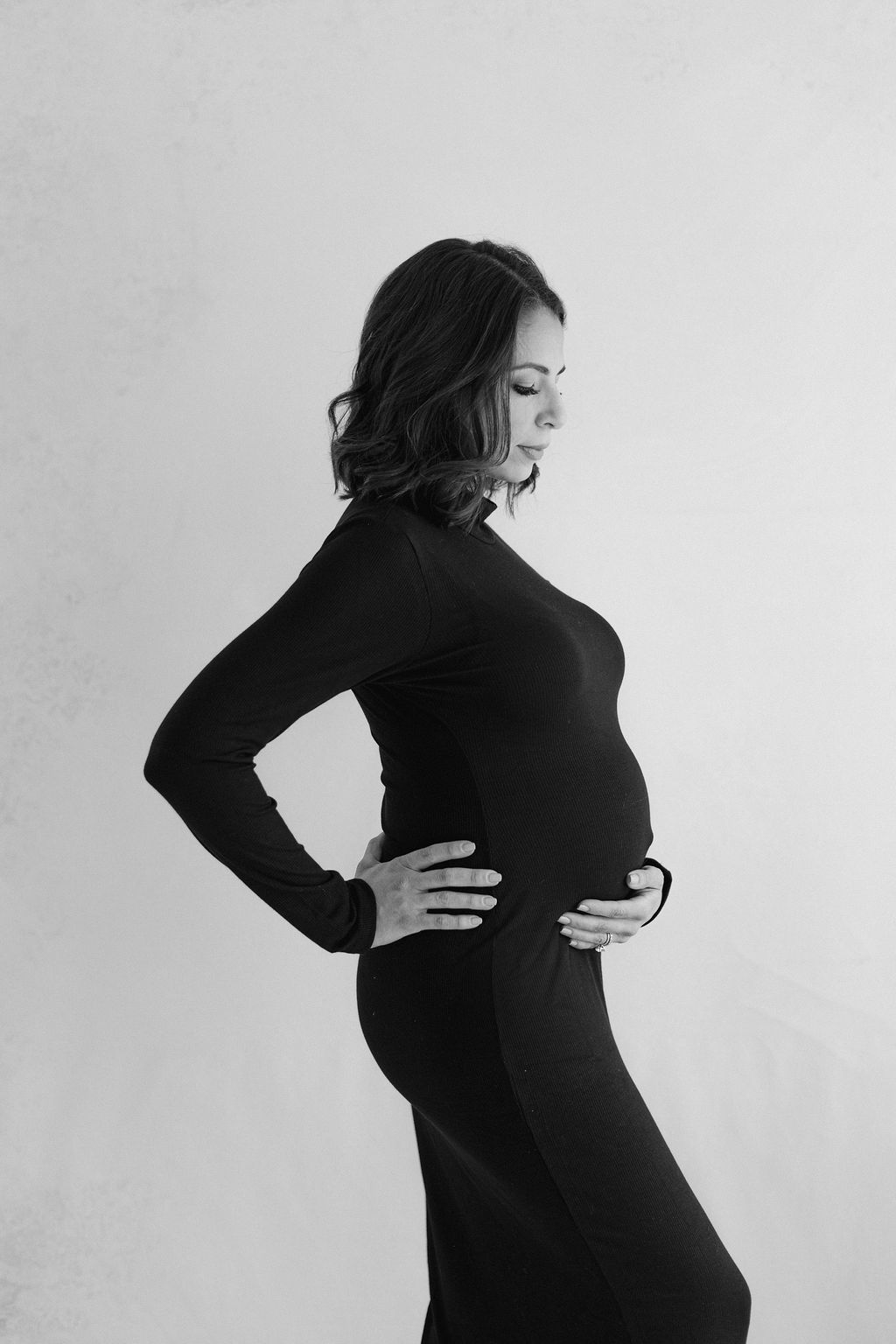 A mother to be wearing a black maternity gown smiles down to her bump