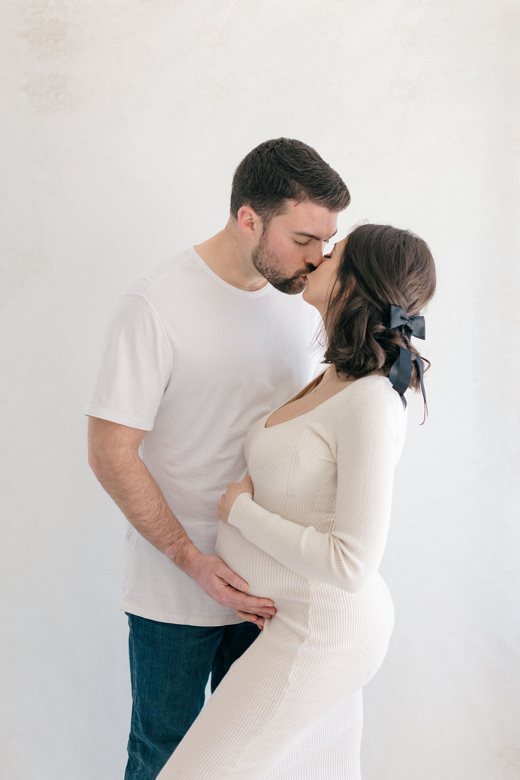 Expecting parents stand in a studio kissing while holding the bump