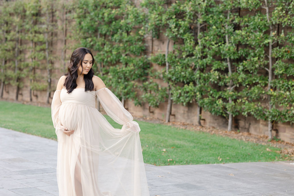 A mom to be in a white maternity gown holds her train while walking on a patio during her Doylestown Maternity photos