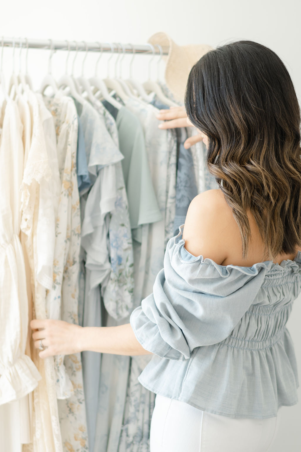 A woman in a blue top looks through a rack of dresses in a studio