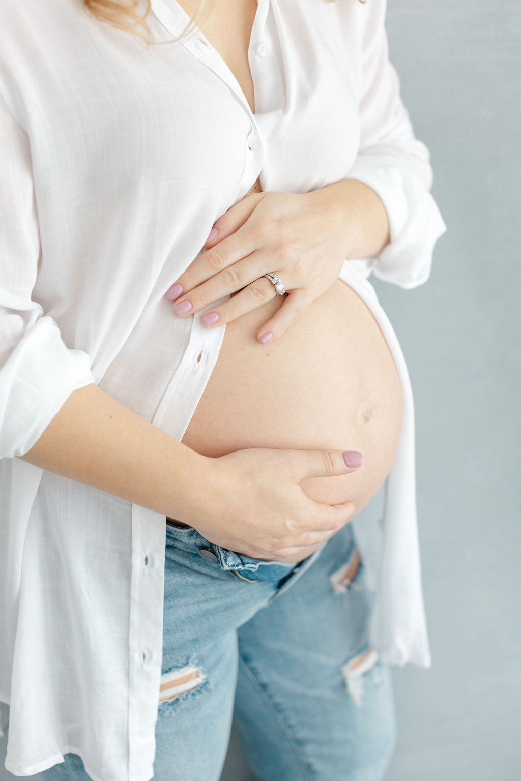 Details of a pregnant woman in an open white shirt holding her bump for some Doylestown Maternity portraits