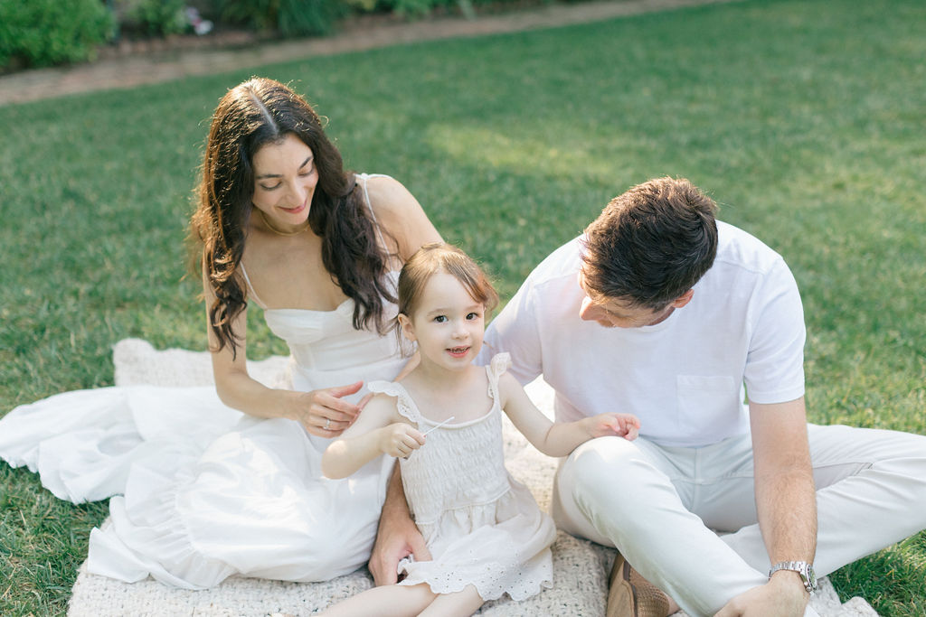 A happy toddler in a white dress sits with mom and dad on a picnic blanket before some ice cream bucks county