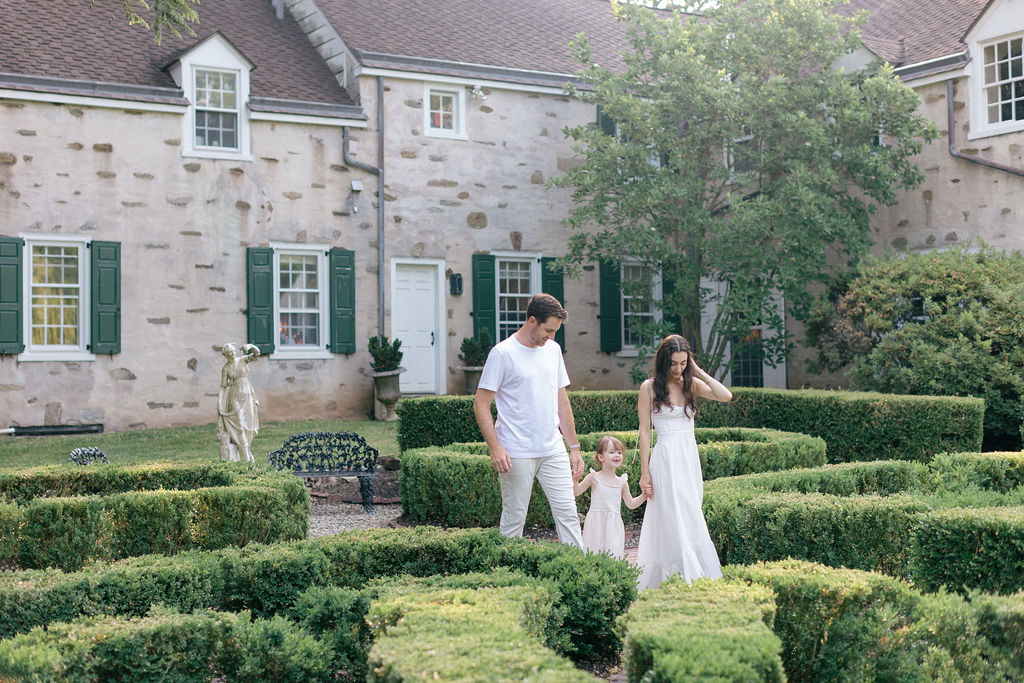 A toddler girl explores a large garden while holding hands with mom and dad before some ice cream bucks county