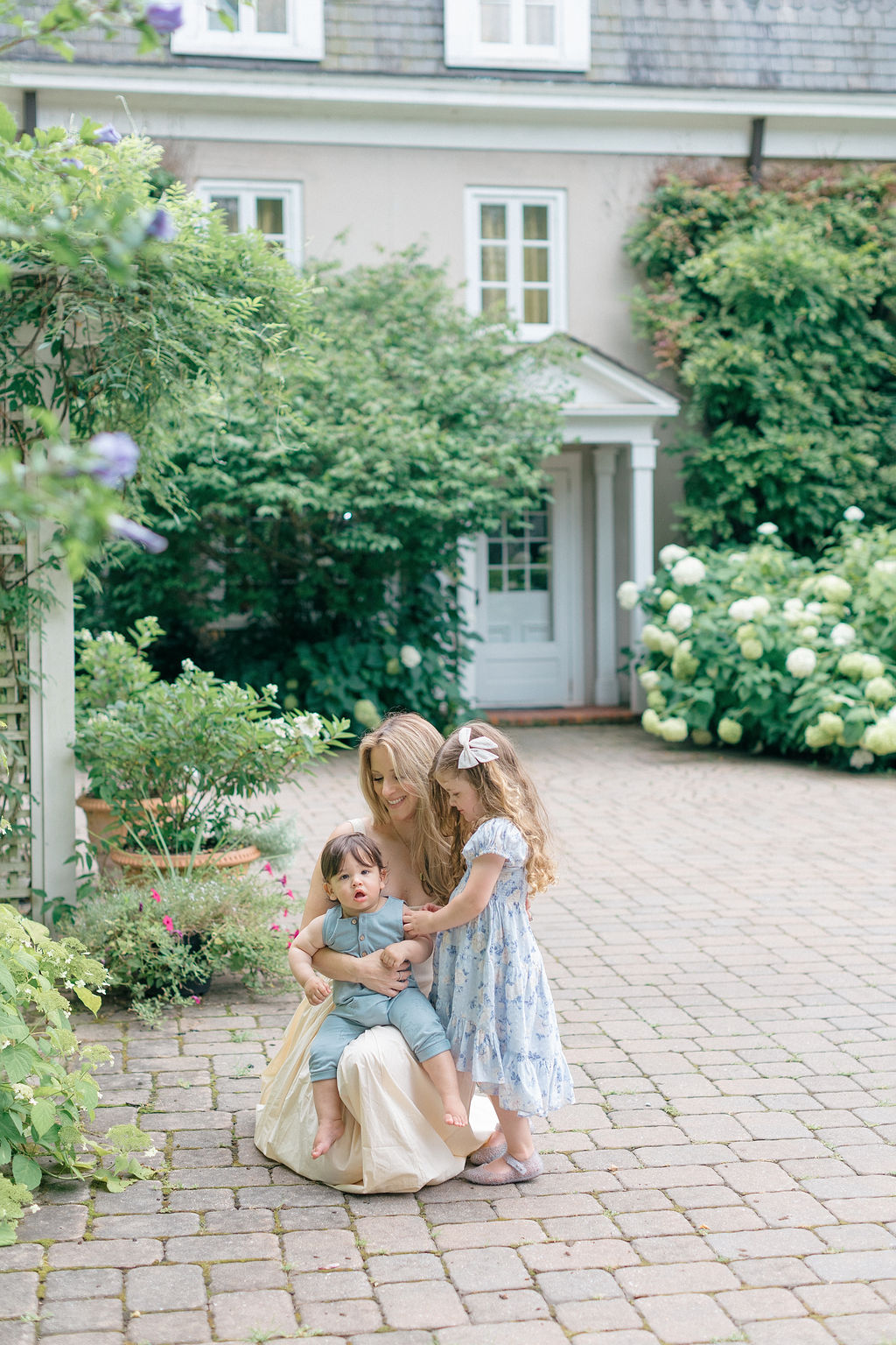 A happy mom explores a garden with her toddler son and daughter in blue outfits