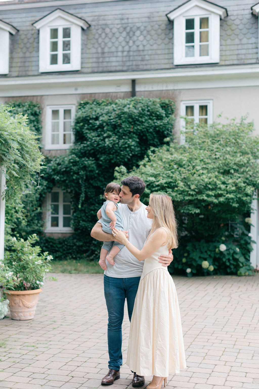 Happy mom and dad stand in a garden patio holding their happy toddler son