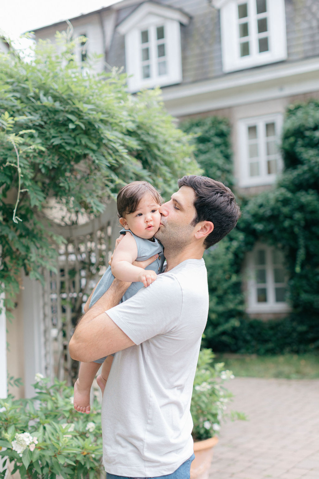 A father kisses the cheek of his young toddler while standing in a garden before visiting pumpkin patches philadelphia