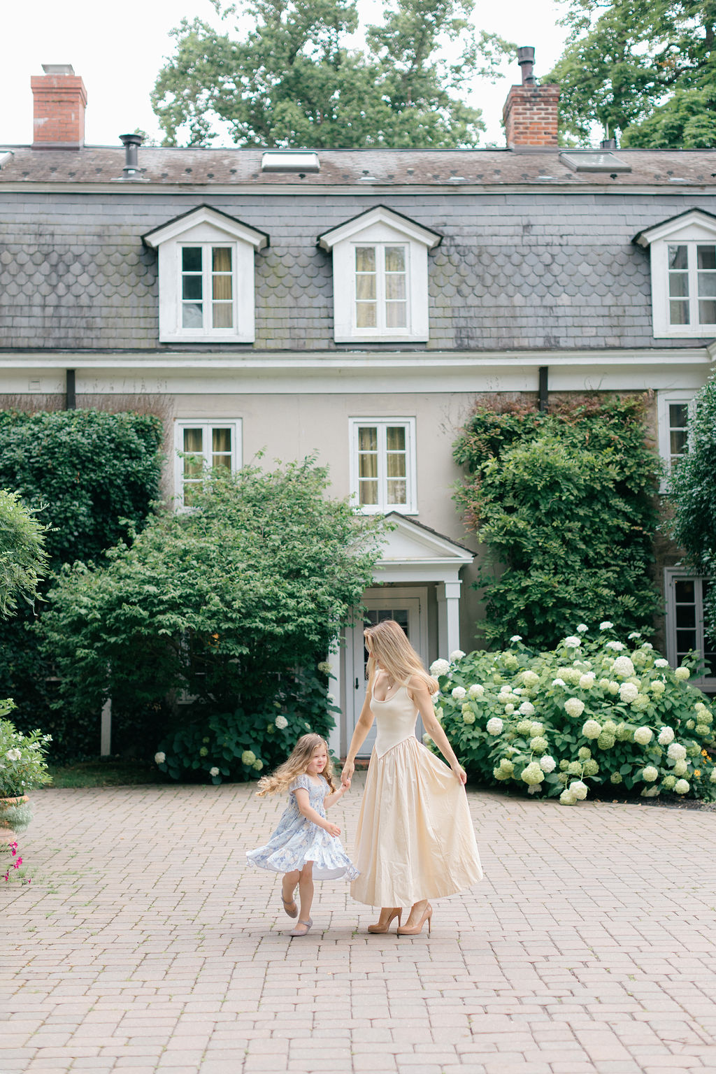 A mother in a yellow dress dances on a paved patio in a garden with her toddler daughter before visiting pumpkin patches philadelphia