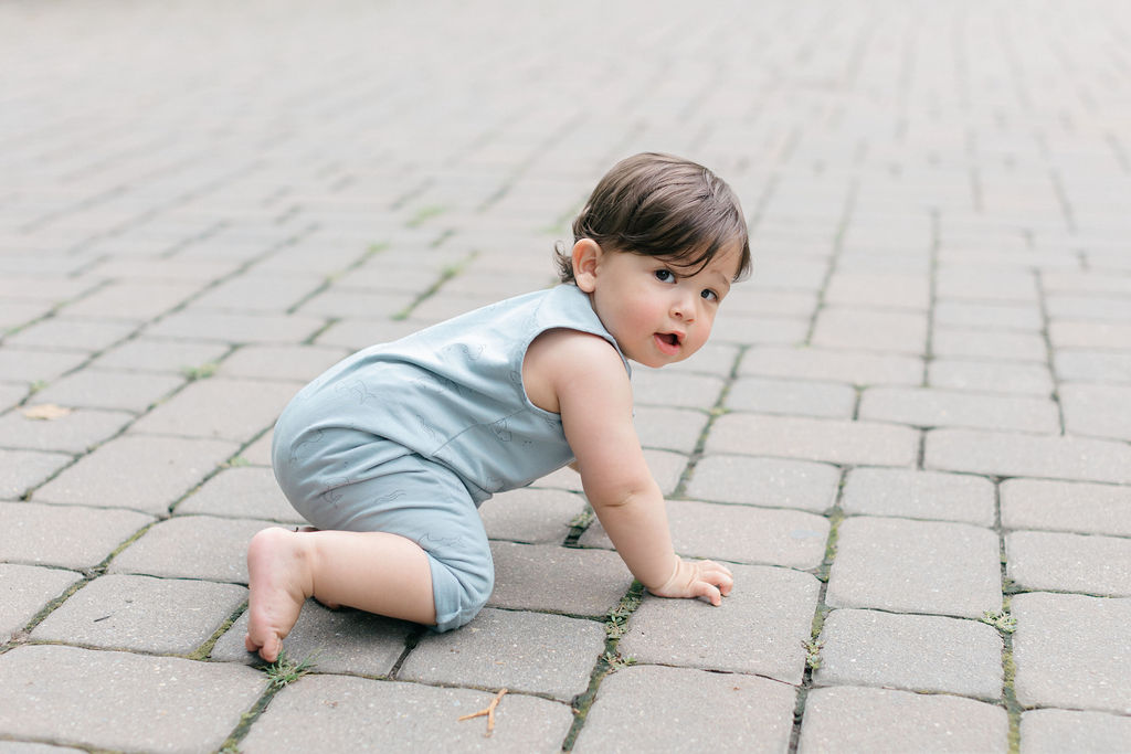 A young toddler in a blue onesie crawls on a stone paved patio before visiting pumpkin patches philadelphia