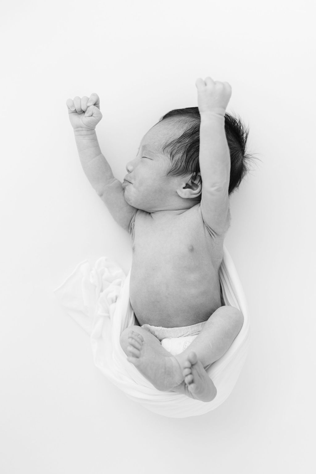 A newborn baby stretches while laying in an open white swaddle in a studio after visiting toy stores main line pa