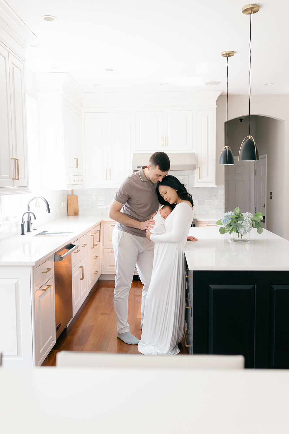 mom and dad holding newborn baby in kitchen