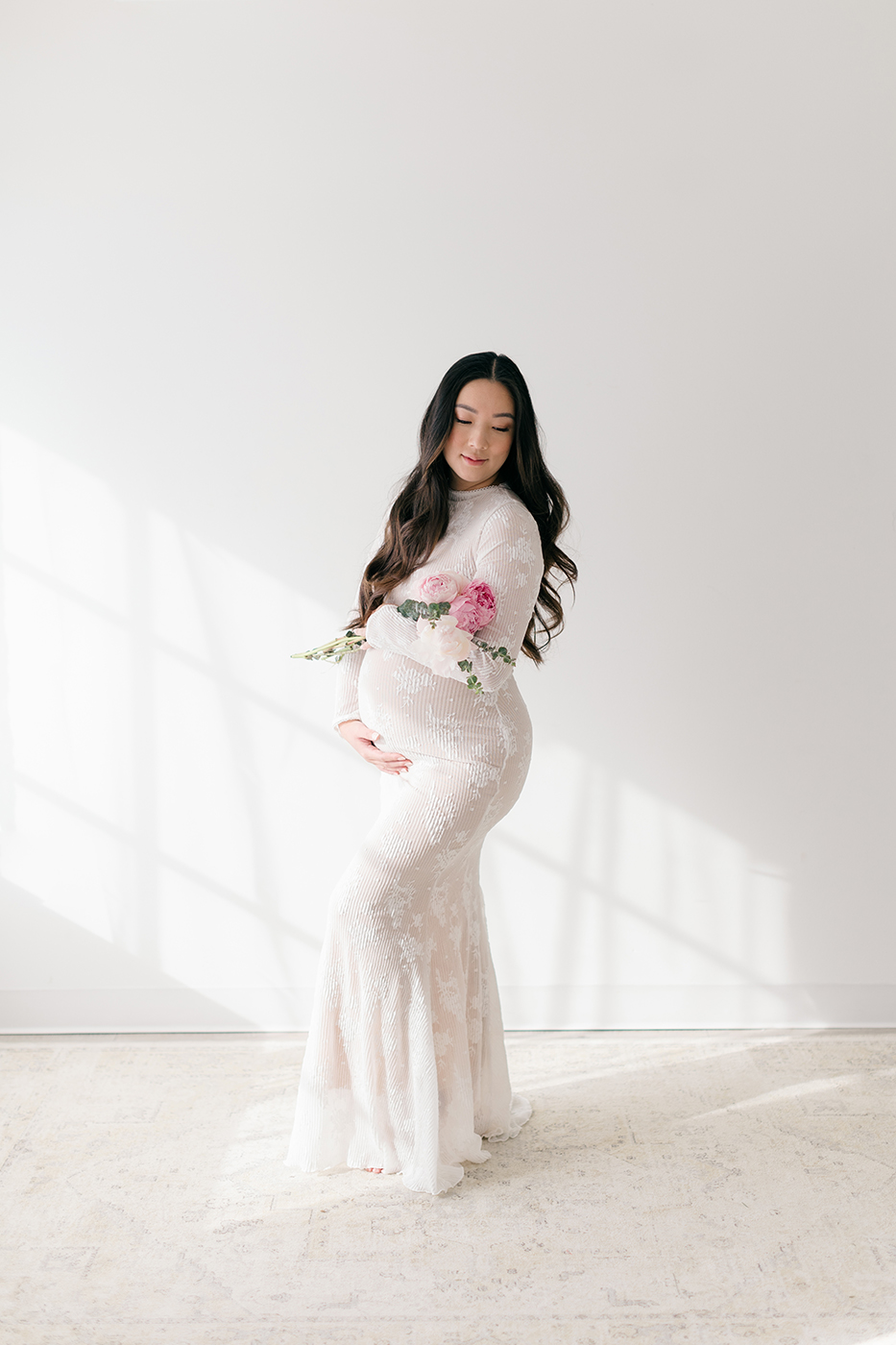 mom-to-be in white lace dress holding pink florals
