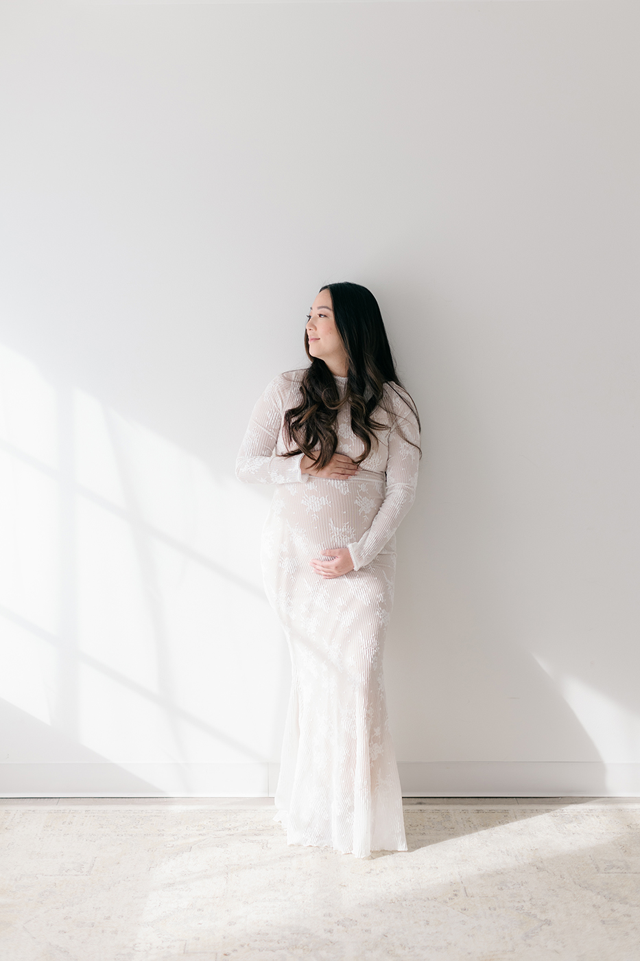 pregnant mom looking out window white lace dress holding belly 