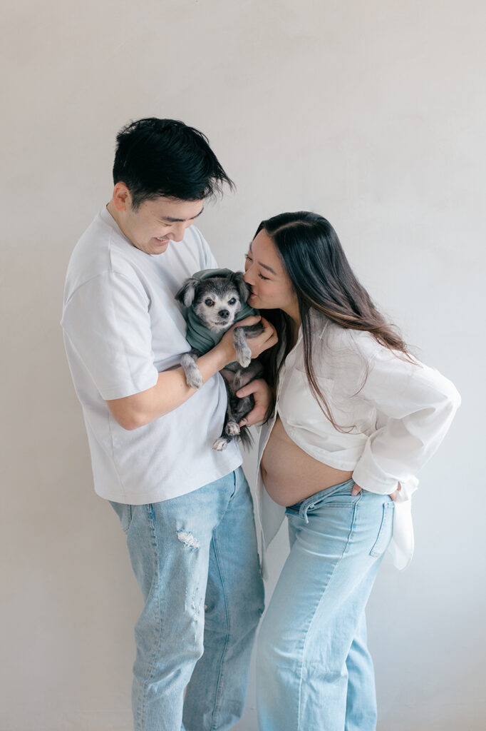 mom-to-be kissing dog expecting couple in jeans and white top