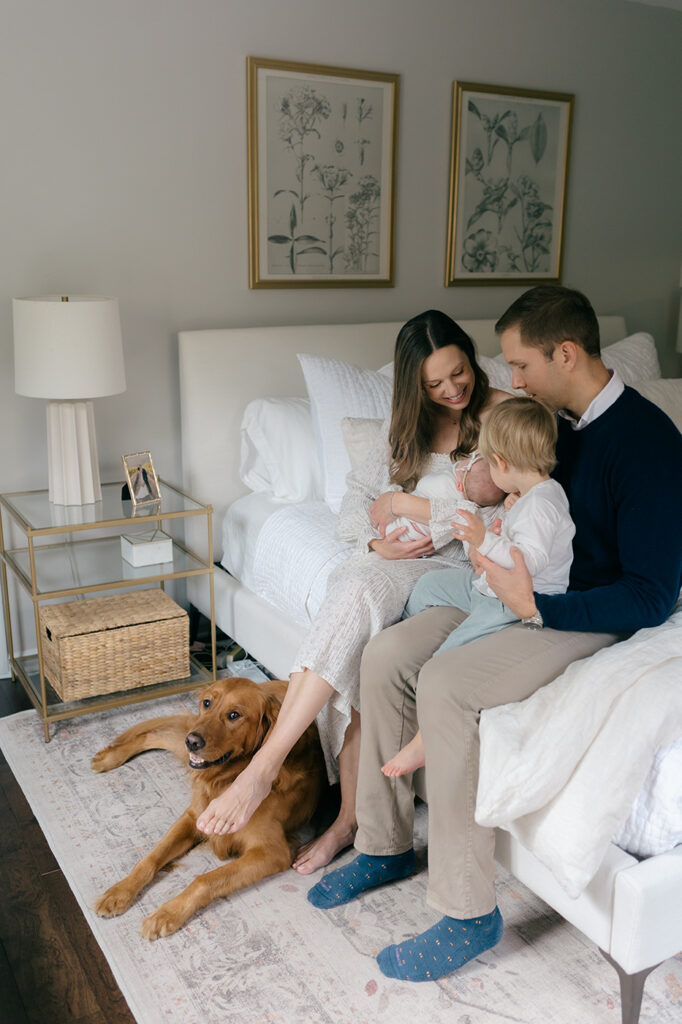 family sitting bed snuggling newborn toddler dog