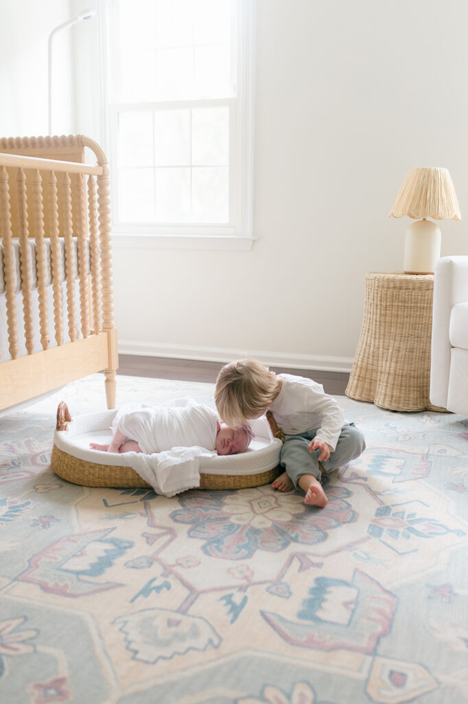 brother kissing newborn sister in nursery moses basket