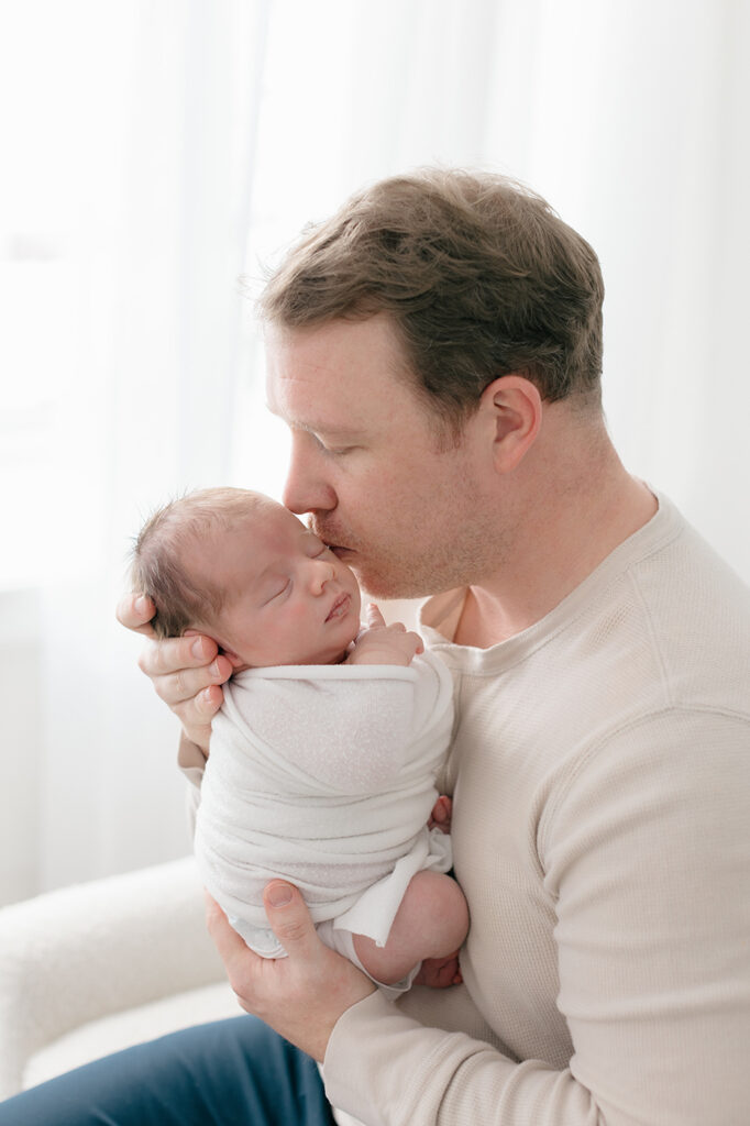 dad kissing newborn baby during lifestyle photography session