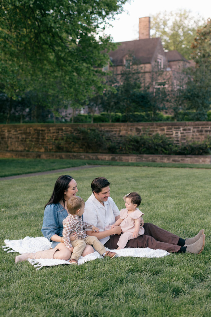 family of 4 sitting on blanket on grass looking at each other
