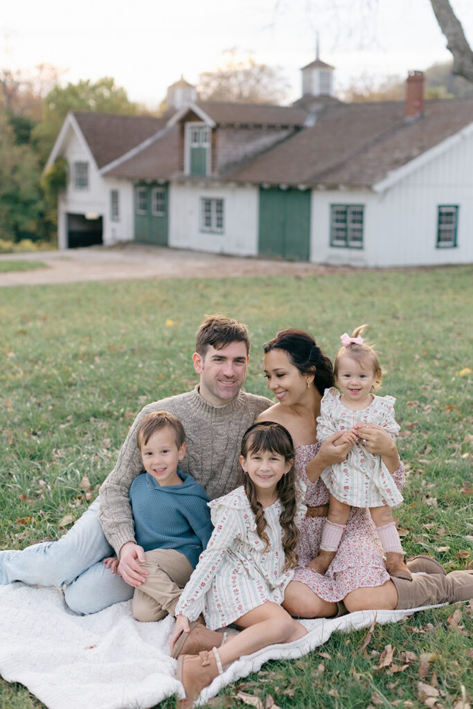 family sitting on grass in front of barn
