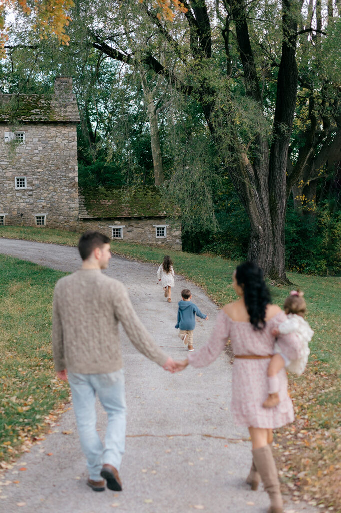 mom and dad holding hands as kids walk ahead park family photos
